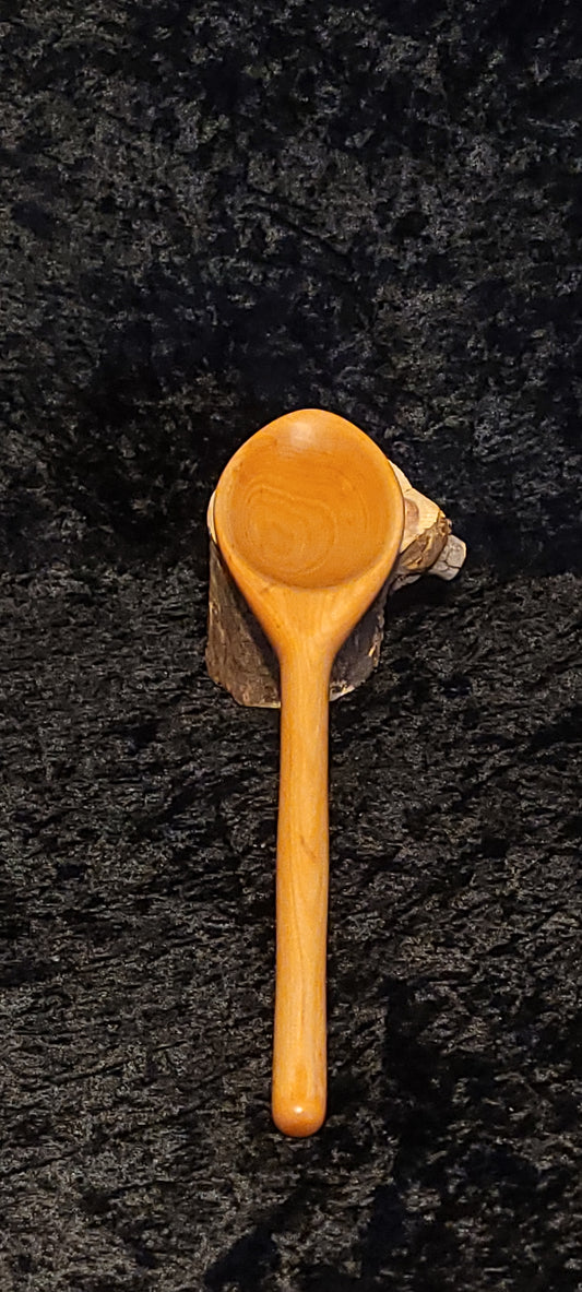 Hand-carved maple wood spoon displayed on a wood slice