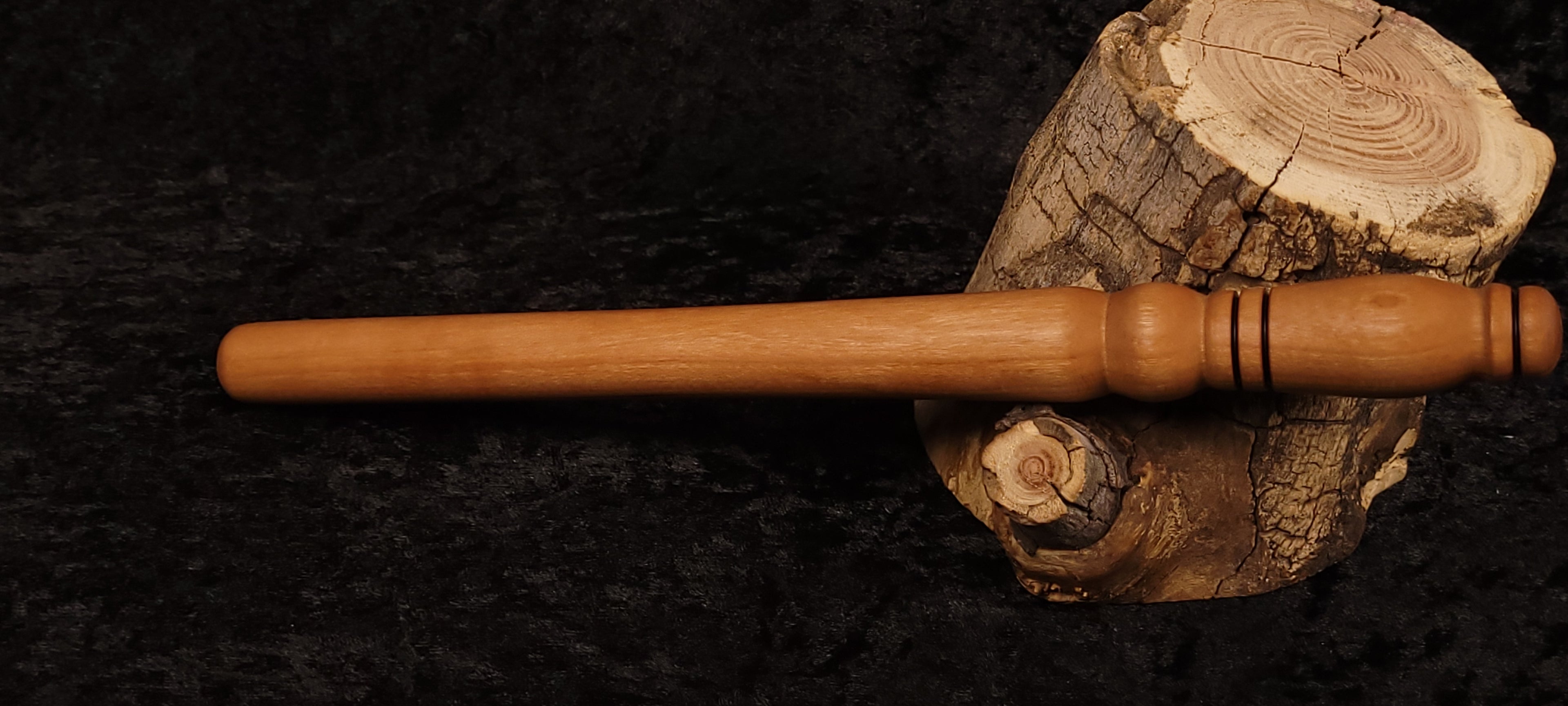 Hand-turned cherry wood rolling pin resting horizontally on log stump
