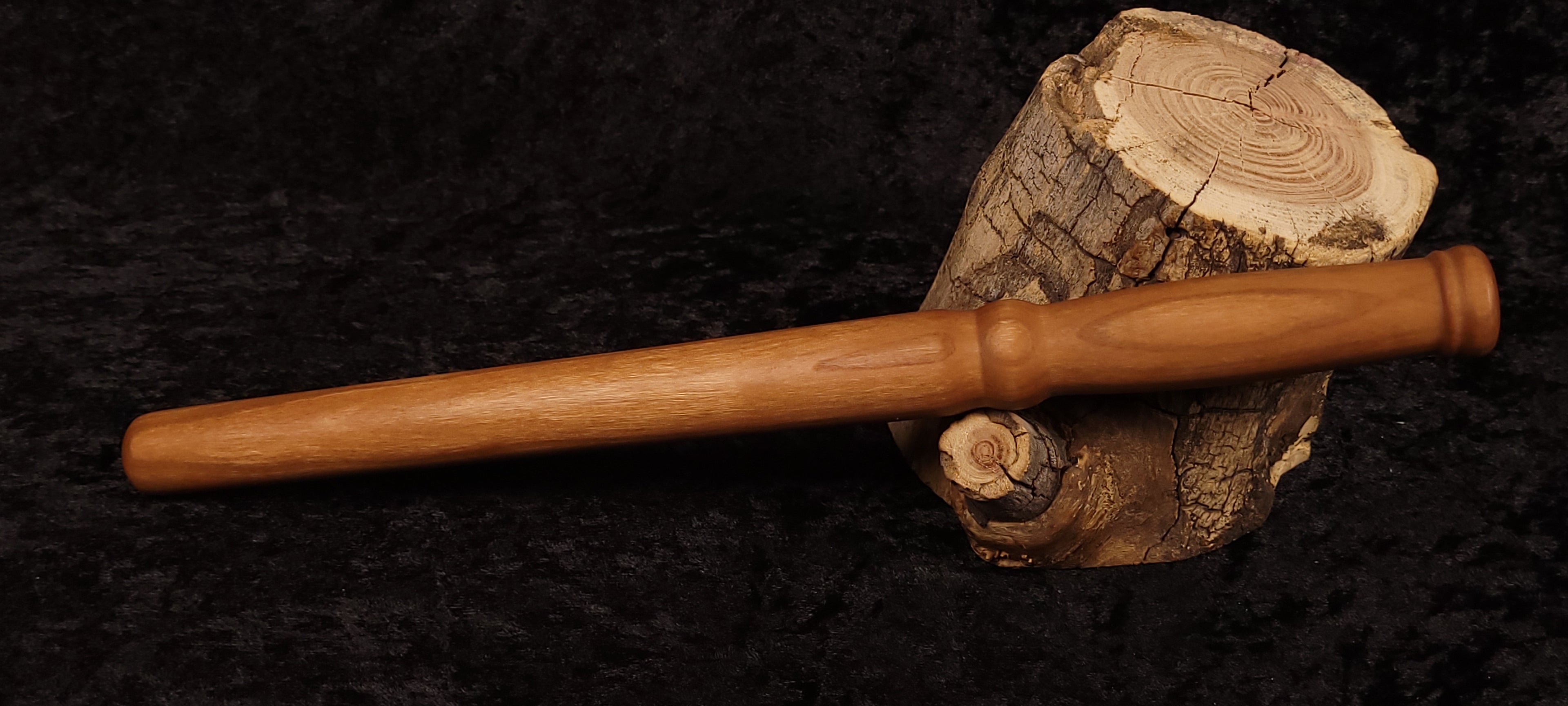 Hand-turned cherry wood spurtle resting horizontally on log stump