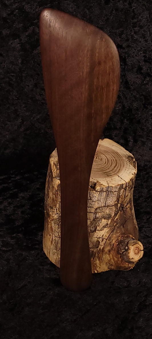 Handcrafted walnut angled spatula front view balanced on log