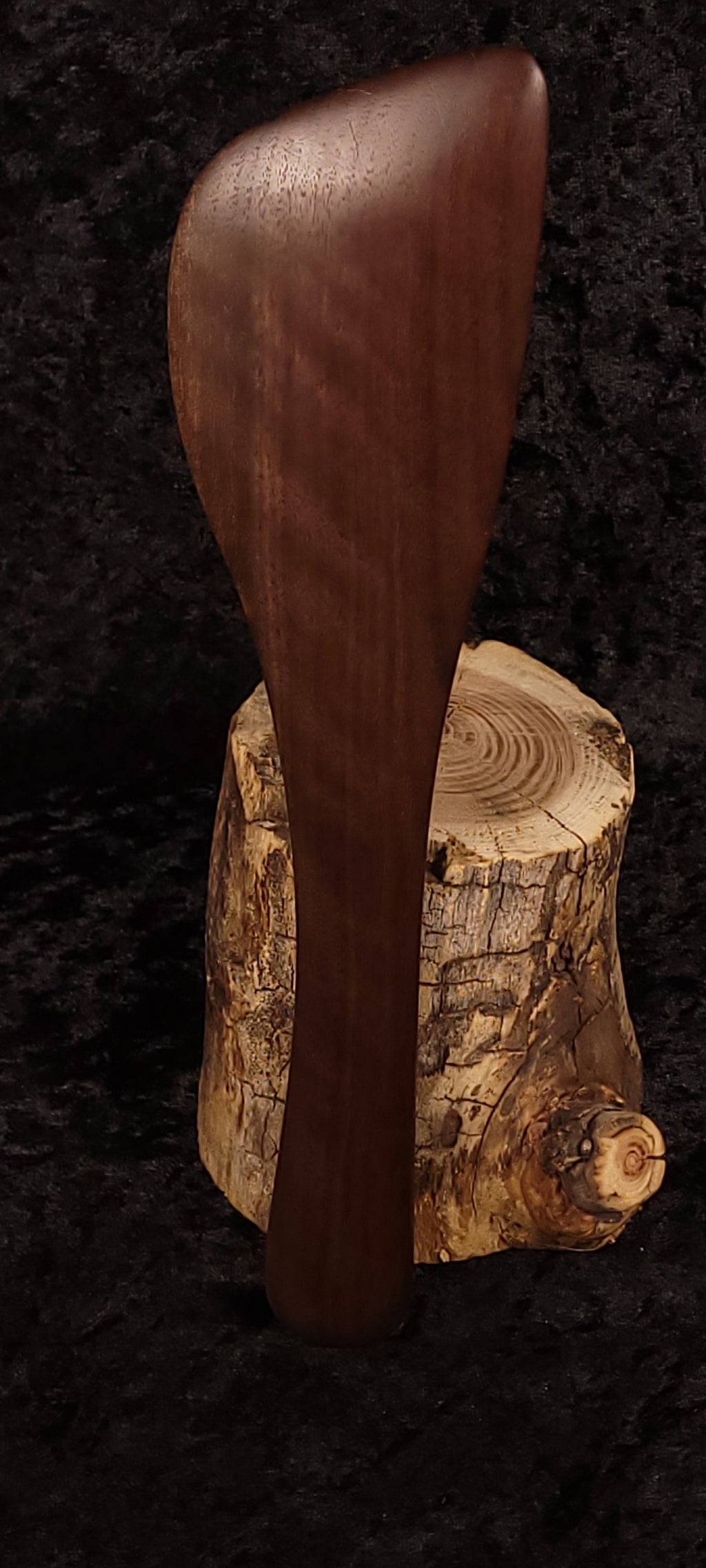 Handcrafted walnut angled spatula side view balanced on log