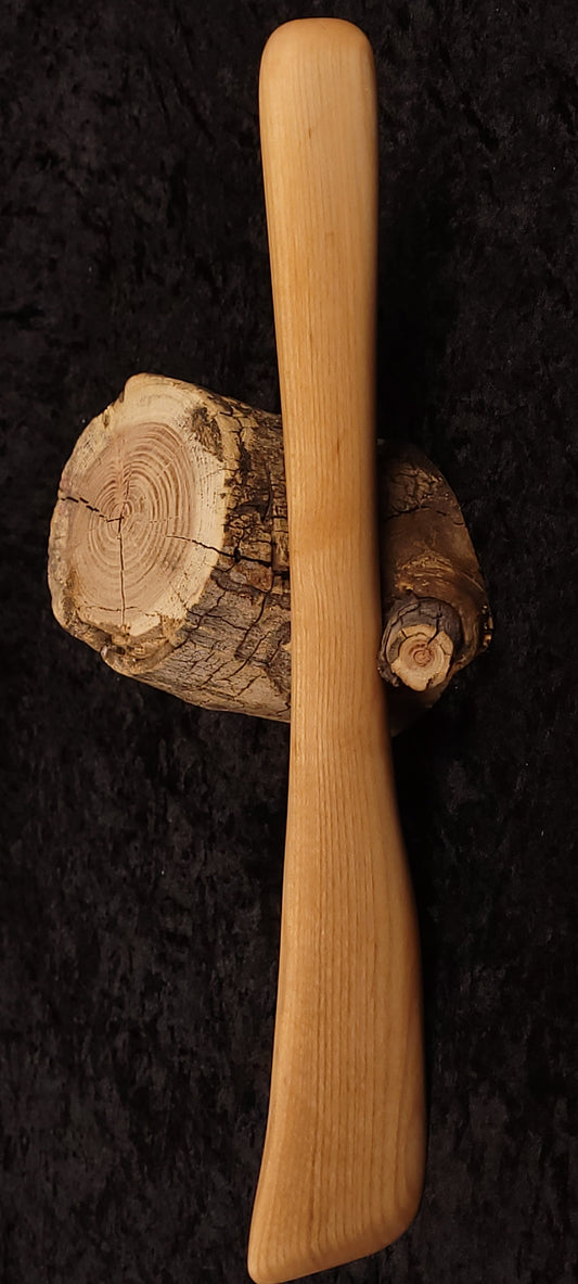 Maple wood spurtle balanced on a log end grain, side view