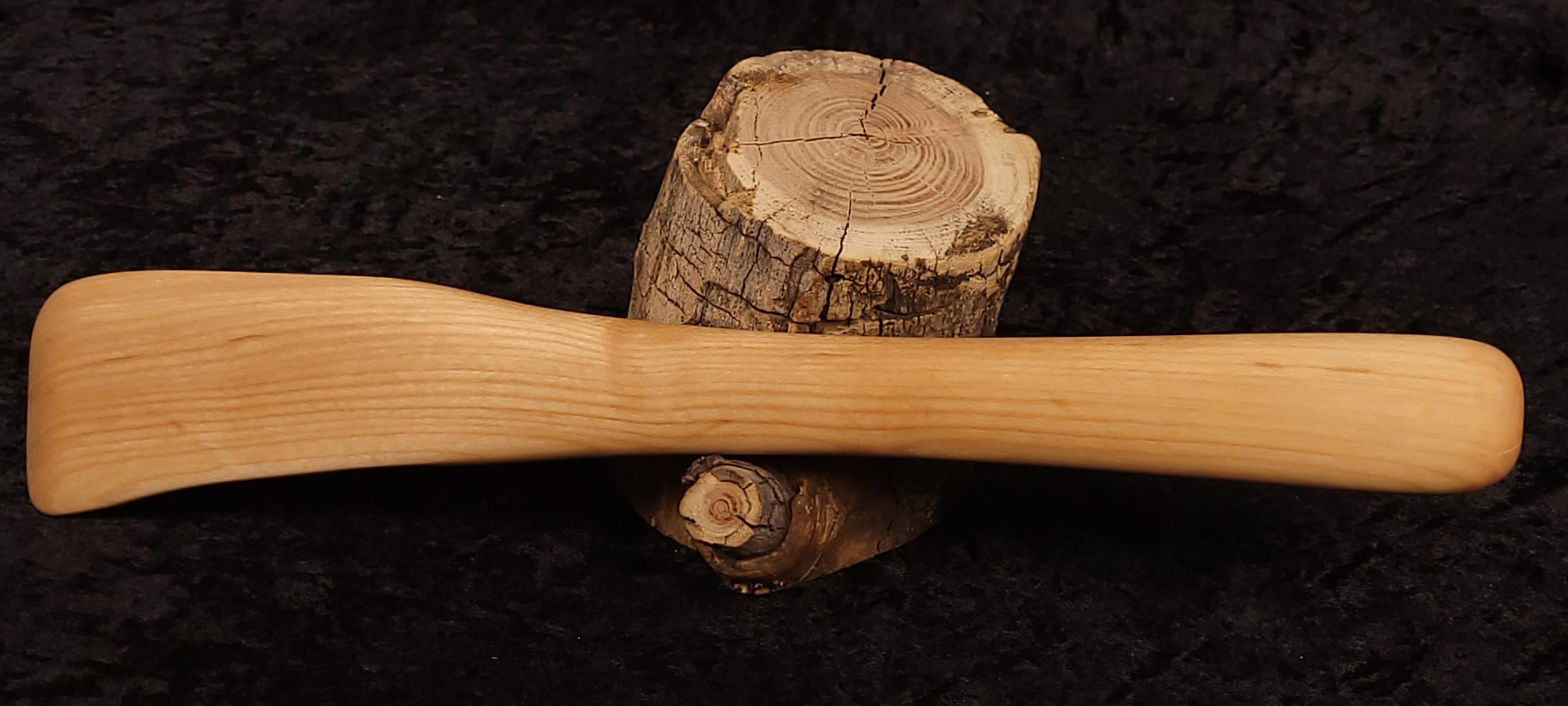 Maple wood spurtle balanced on a log, full length side view