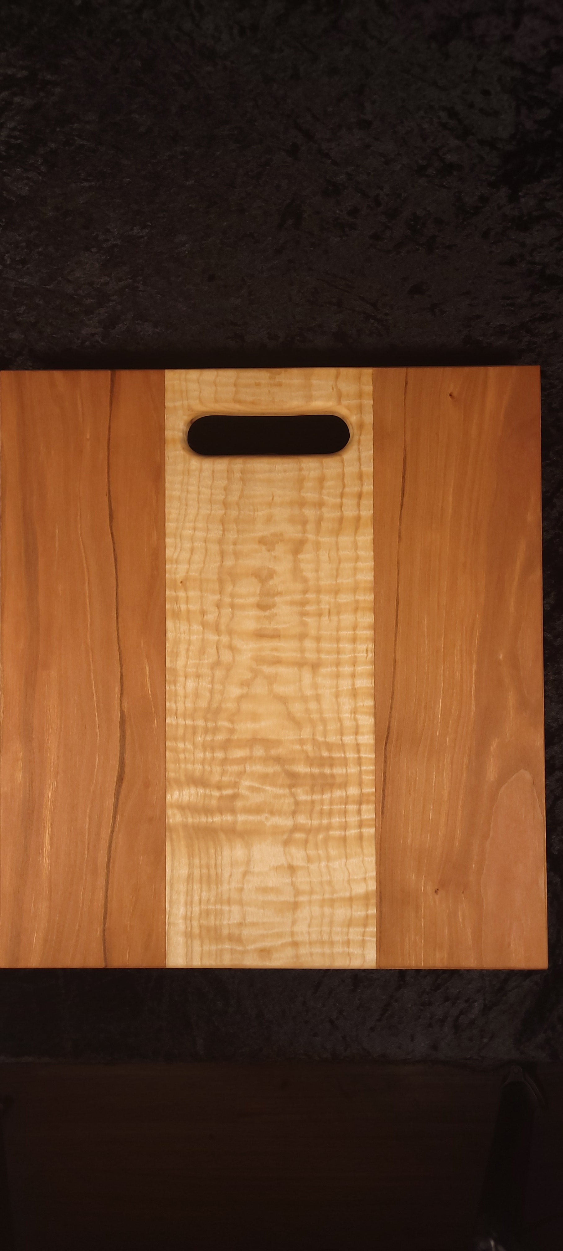 Cherry and curly maple cutting board face showing wide maple center stripe and oval handle