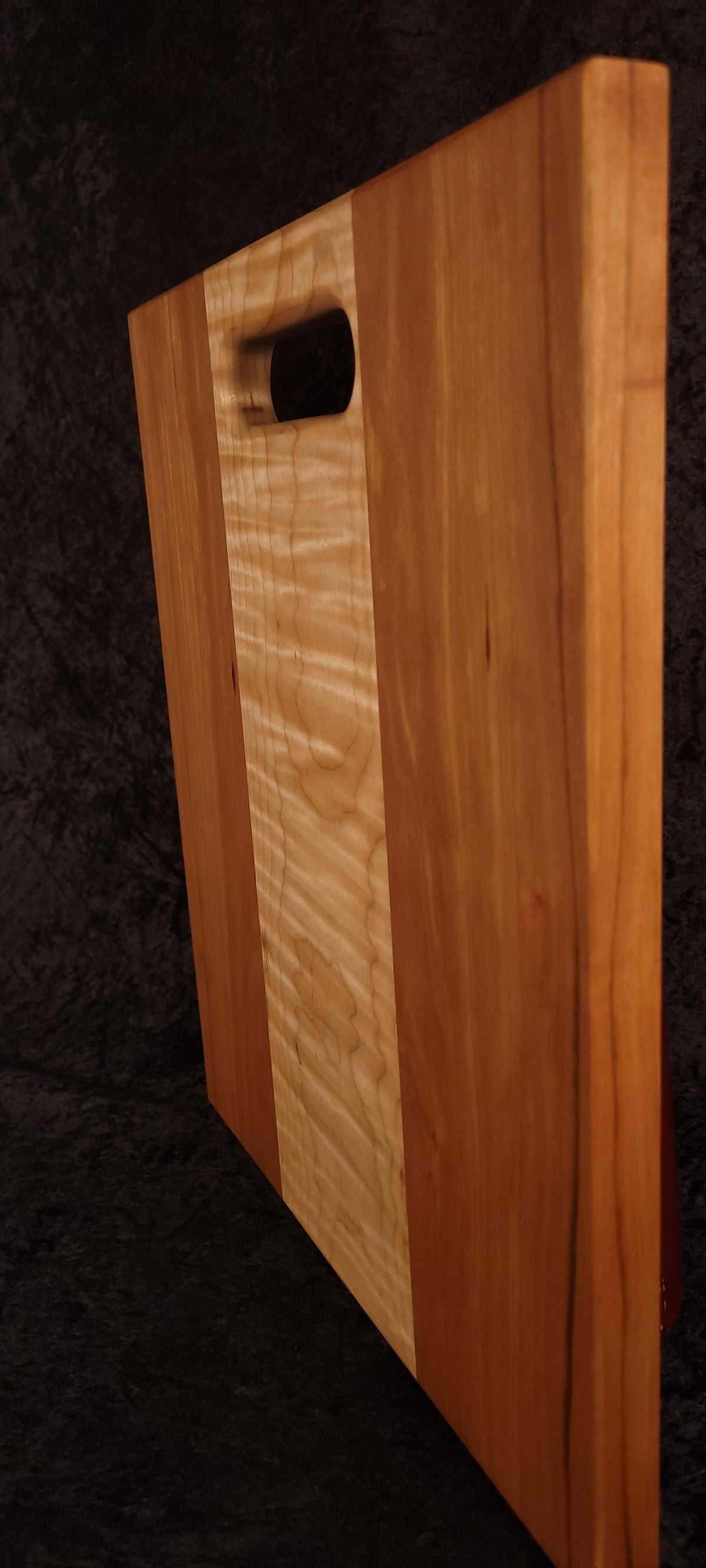 Cutting board standing on edge showing thickness, cherry grain and maple stripe
