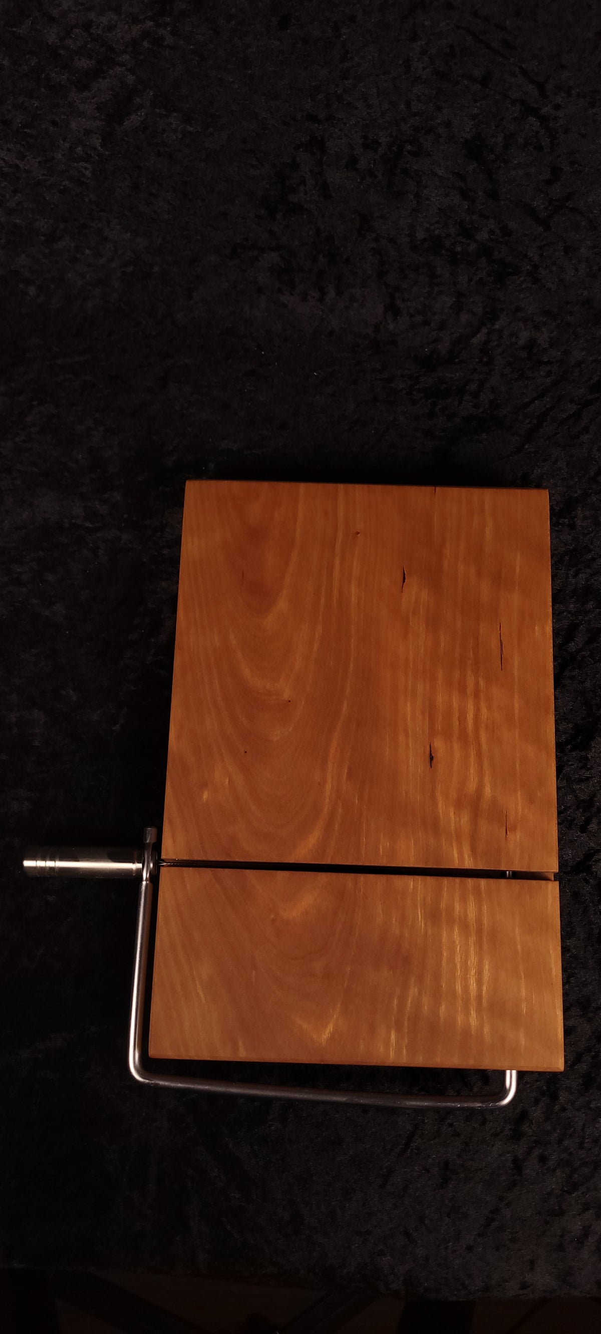 Cherry cheese board angled on wood slice showing stainless wire cutter