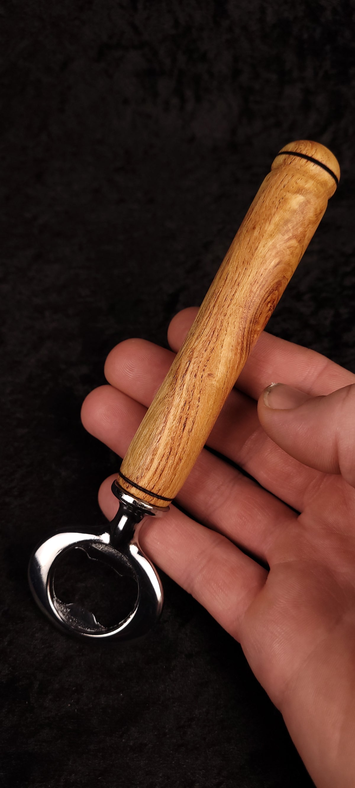 Locust wood bottle opener on dark background, side view