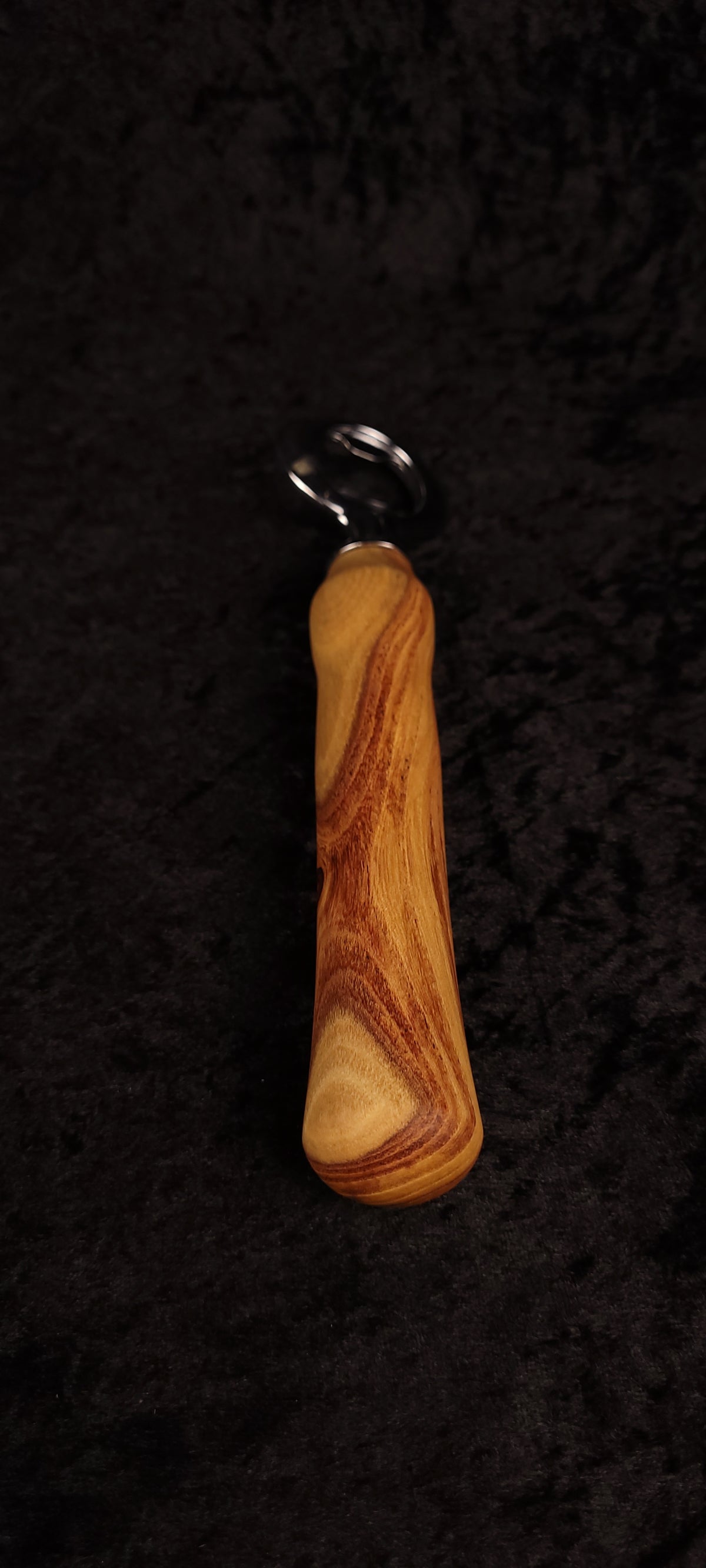 Figured locust wood bottle opener on dark background, top view