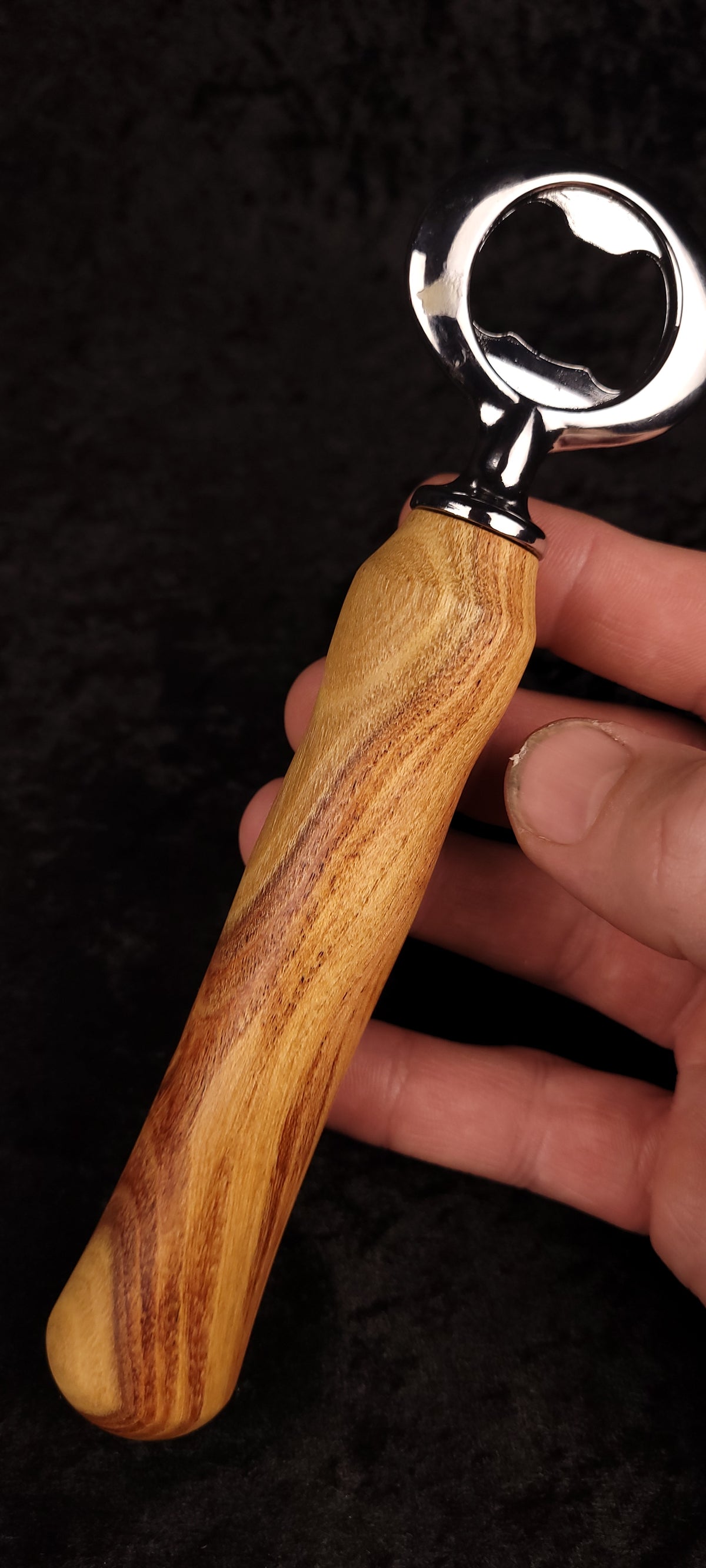 Figured locust wood bottle opener on dark background, side view