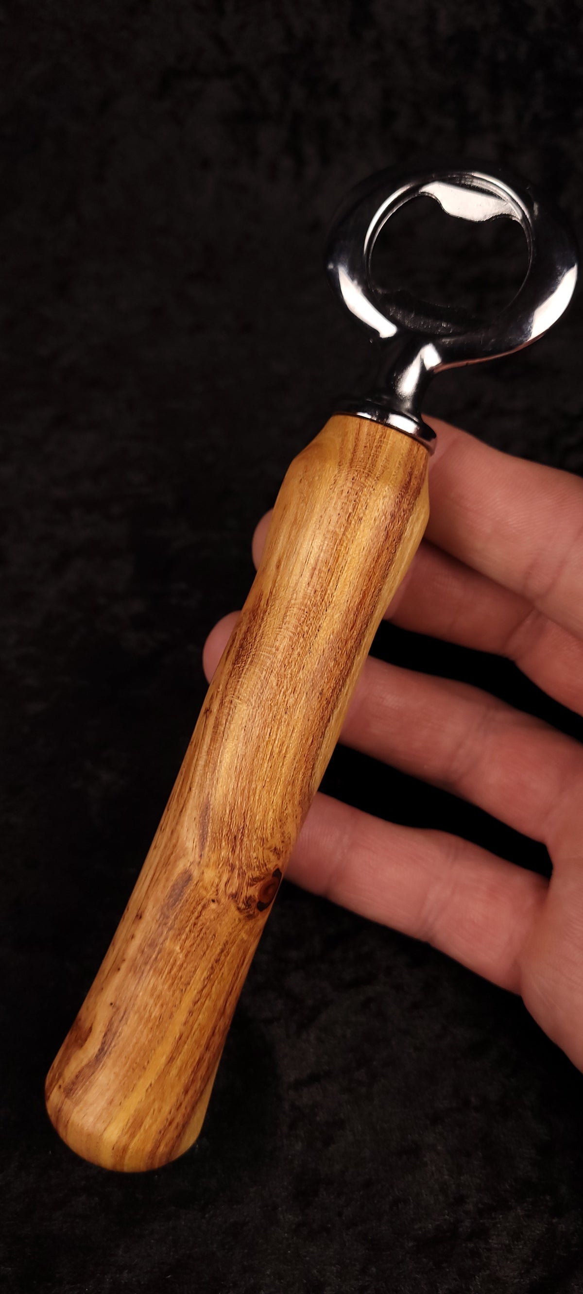 Figured locust wood bottle opener held in hand, full view