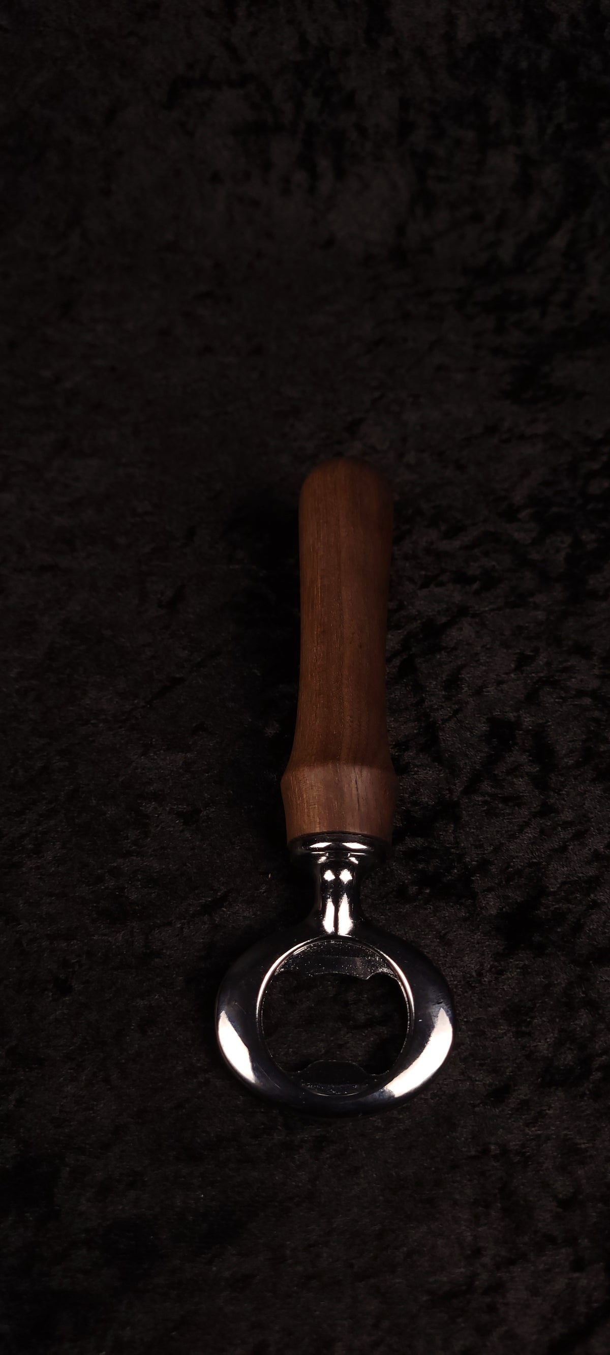 Walnut wood bottle opener on dark background, side view