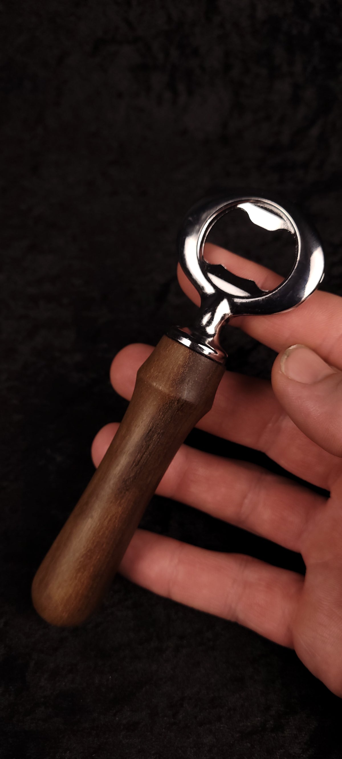 Walnut wood bottle opener held in hand, front view