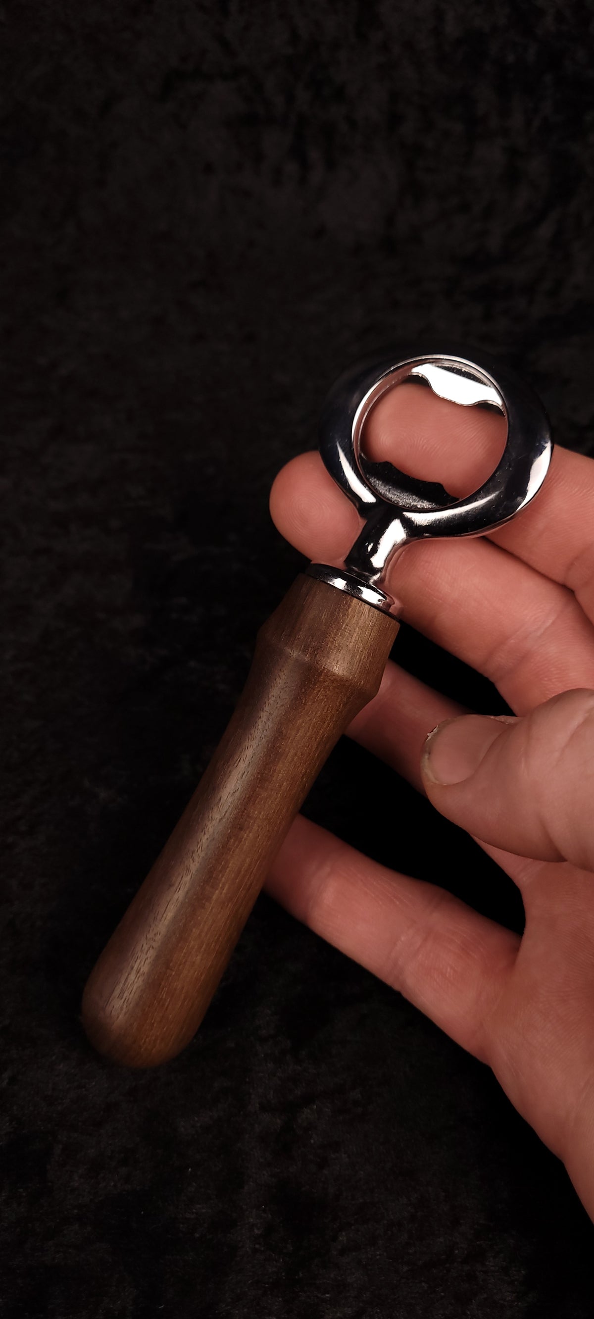 Walnut wood bottle opener held in hand, angled view