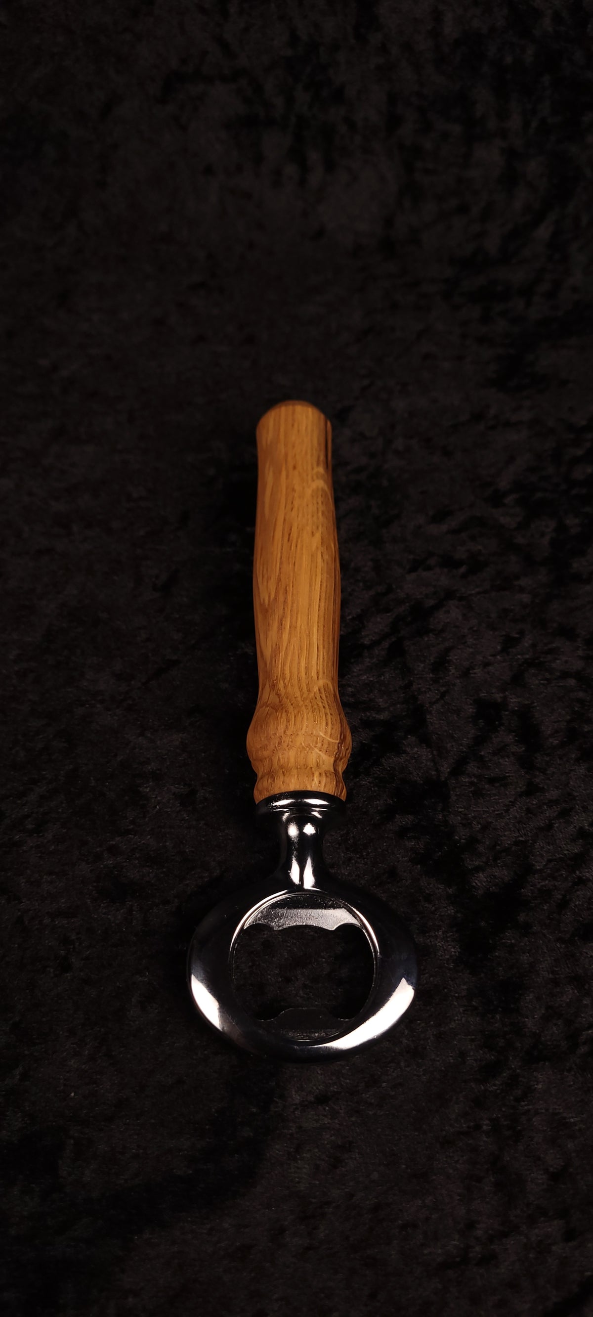 Oak wood bottle opener on dark background, side view