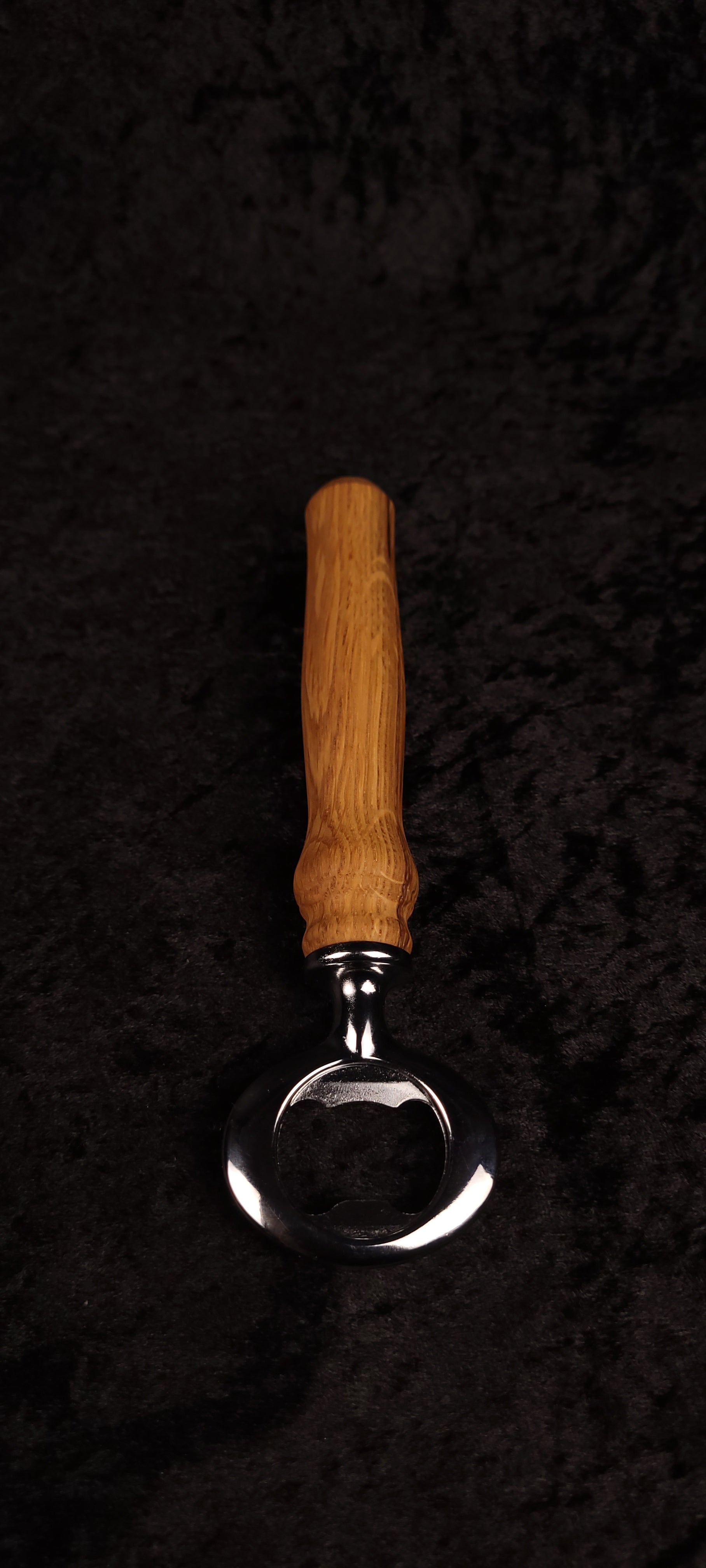 Oak wood bottle opener on dark background, side view