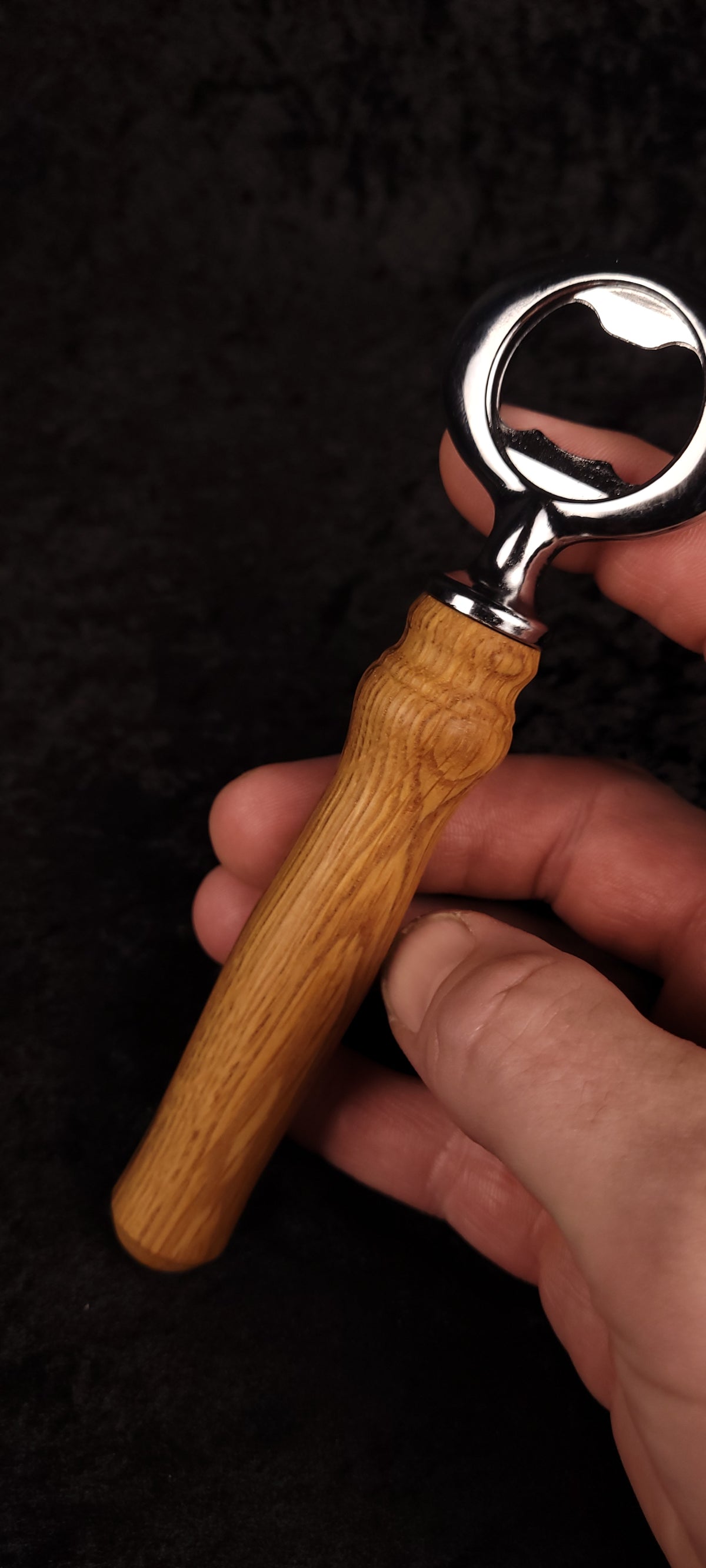 Oak wood bottle opener held in hand, front view