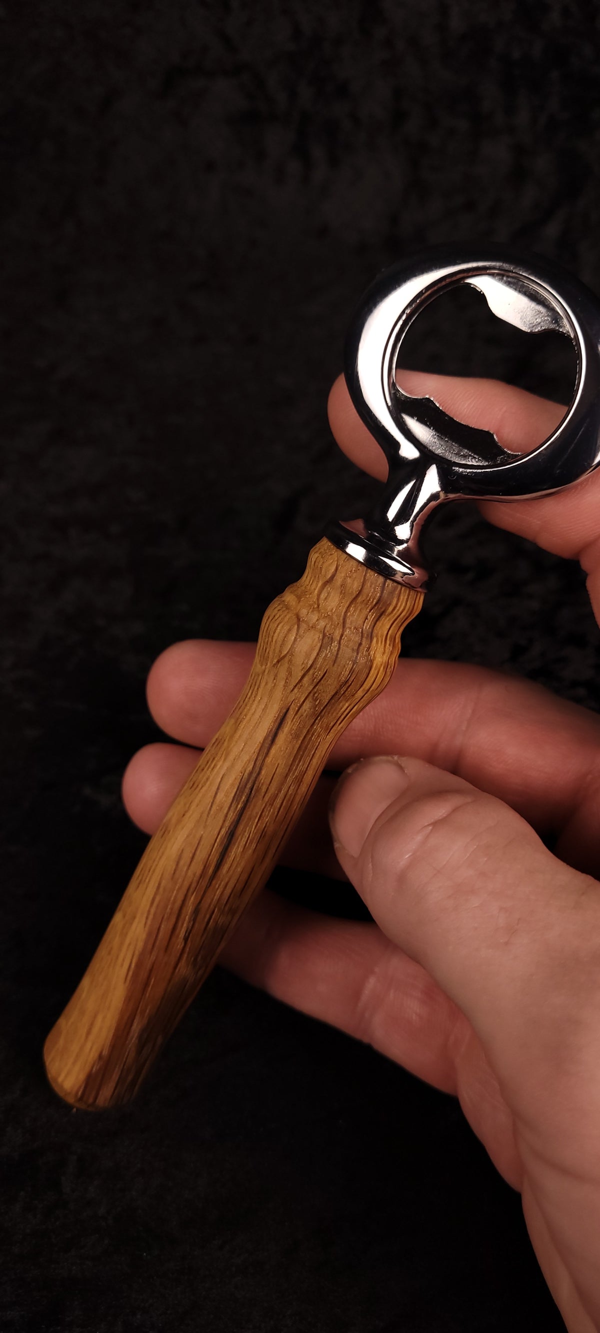 Oak wood bottle opener held in hand, angled view