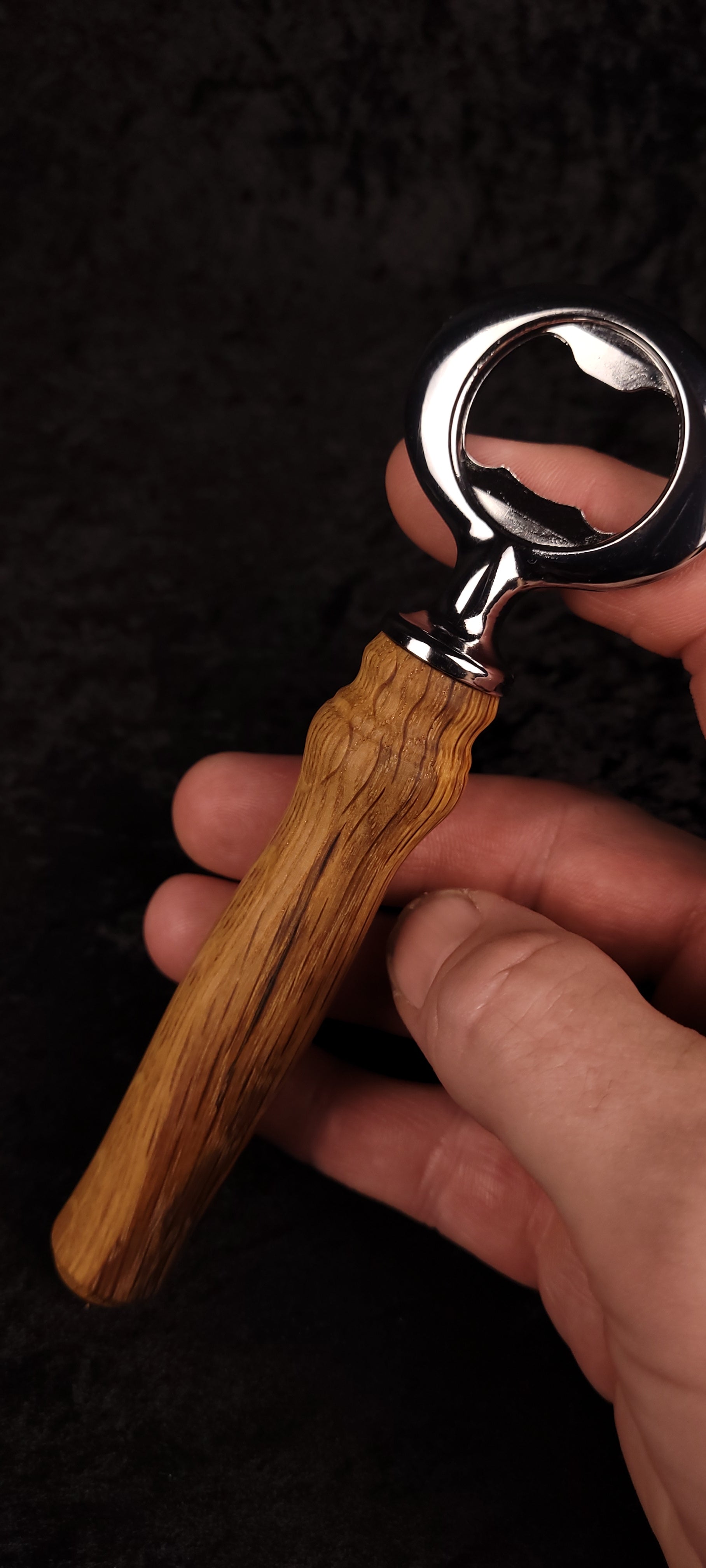 Oak wood bottle opener held in hand, angled view