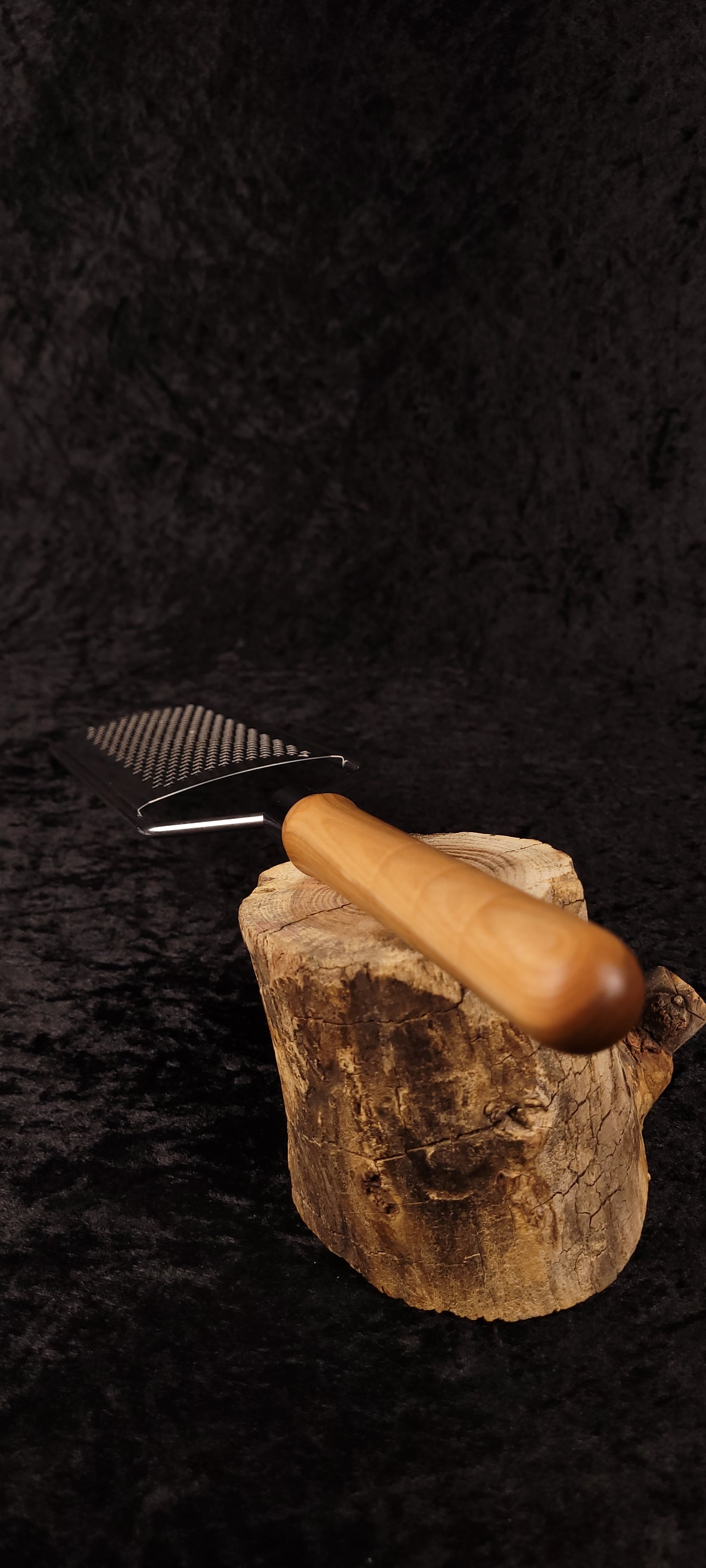 Curly maple rasp grater resting on wood round, side view