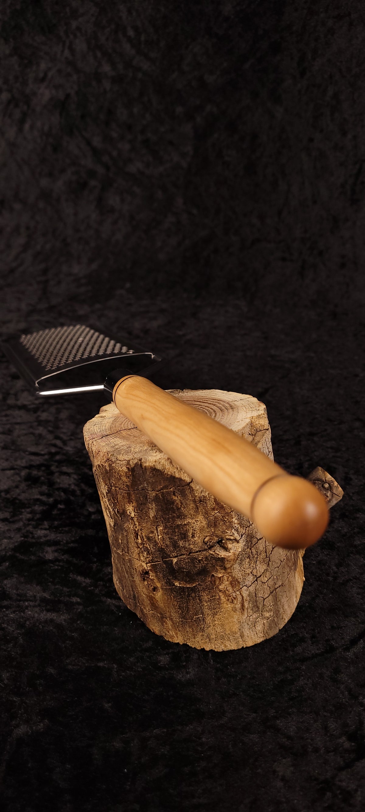 Handcrafted maple flat grater resting on wood round, side view