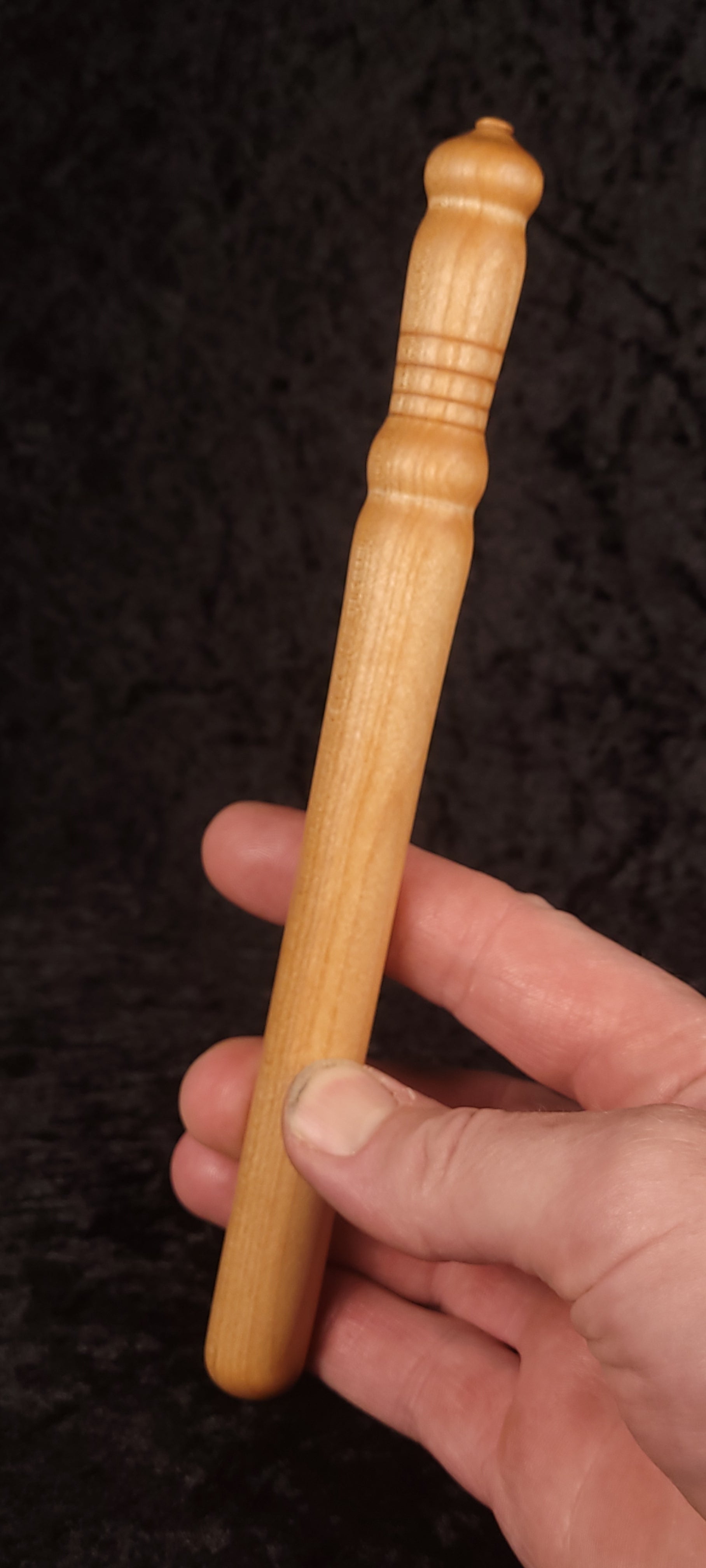 Curly maple spurtle held in hand showing scale and finial top