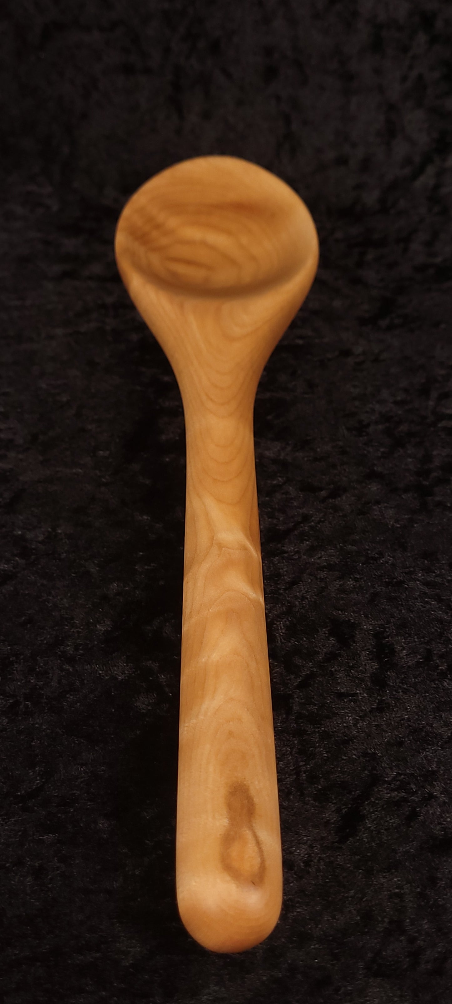 Curly maple spoon angled view on wood round showing full length