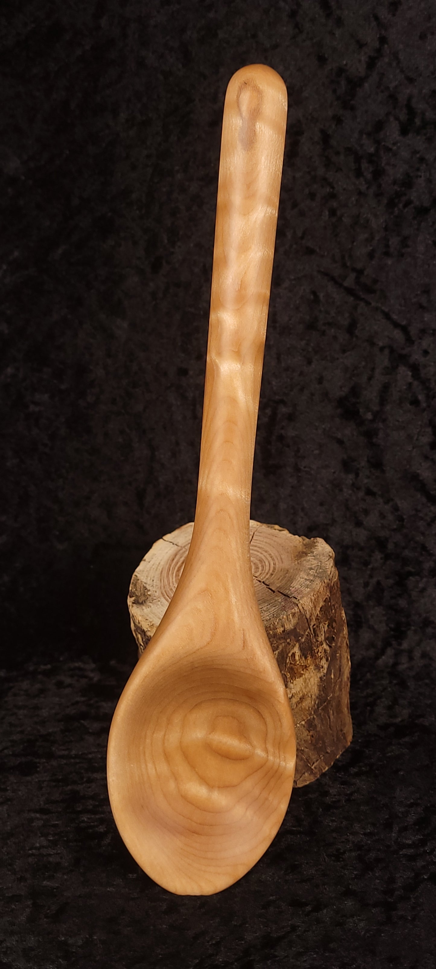 Curly maple spoon side view on wood round showing profile