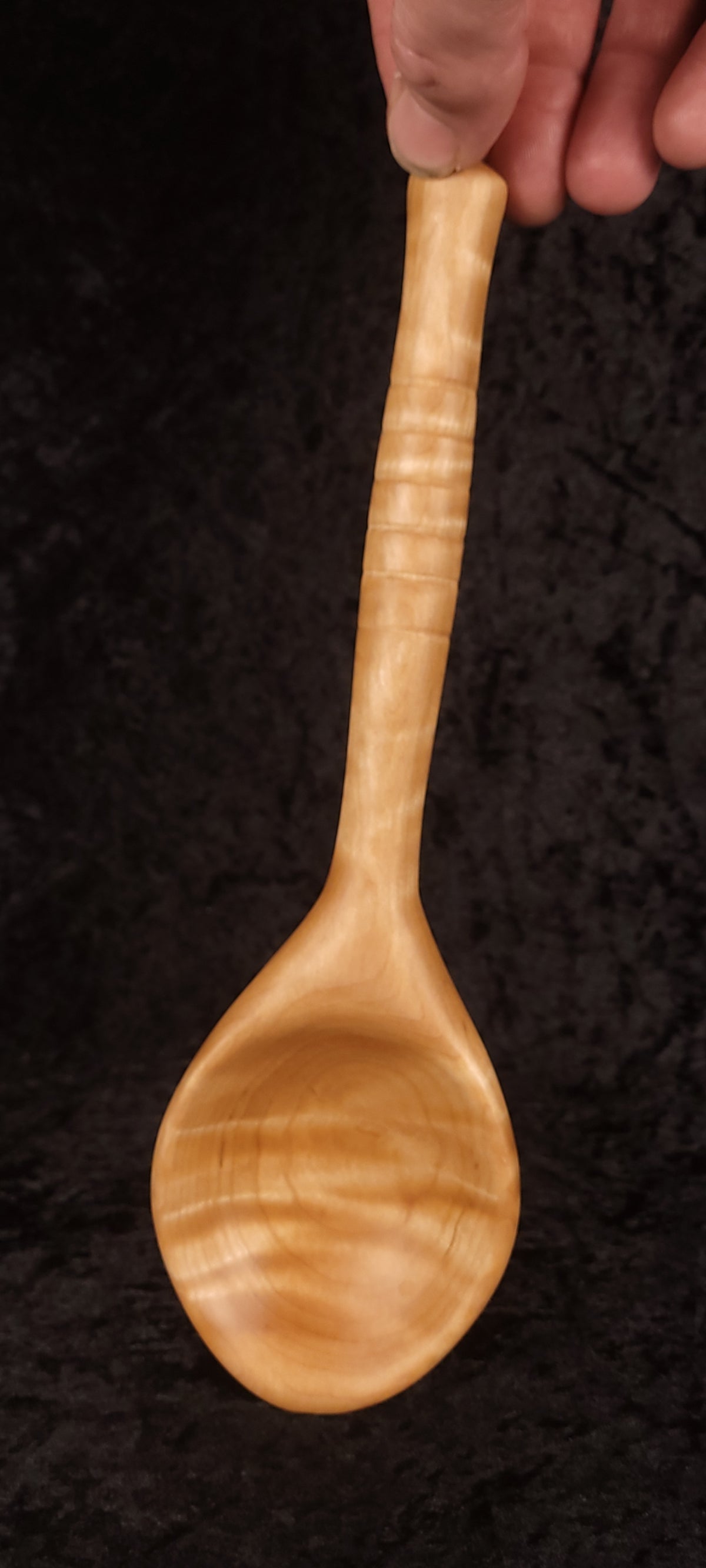 Curly maple spoon held up showing full length and handle detail