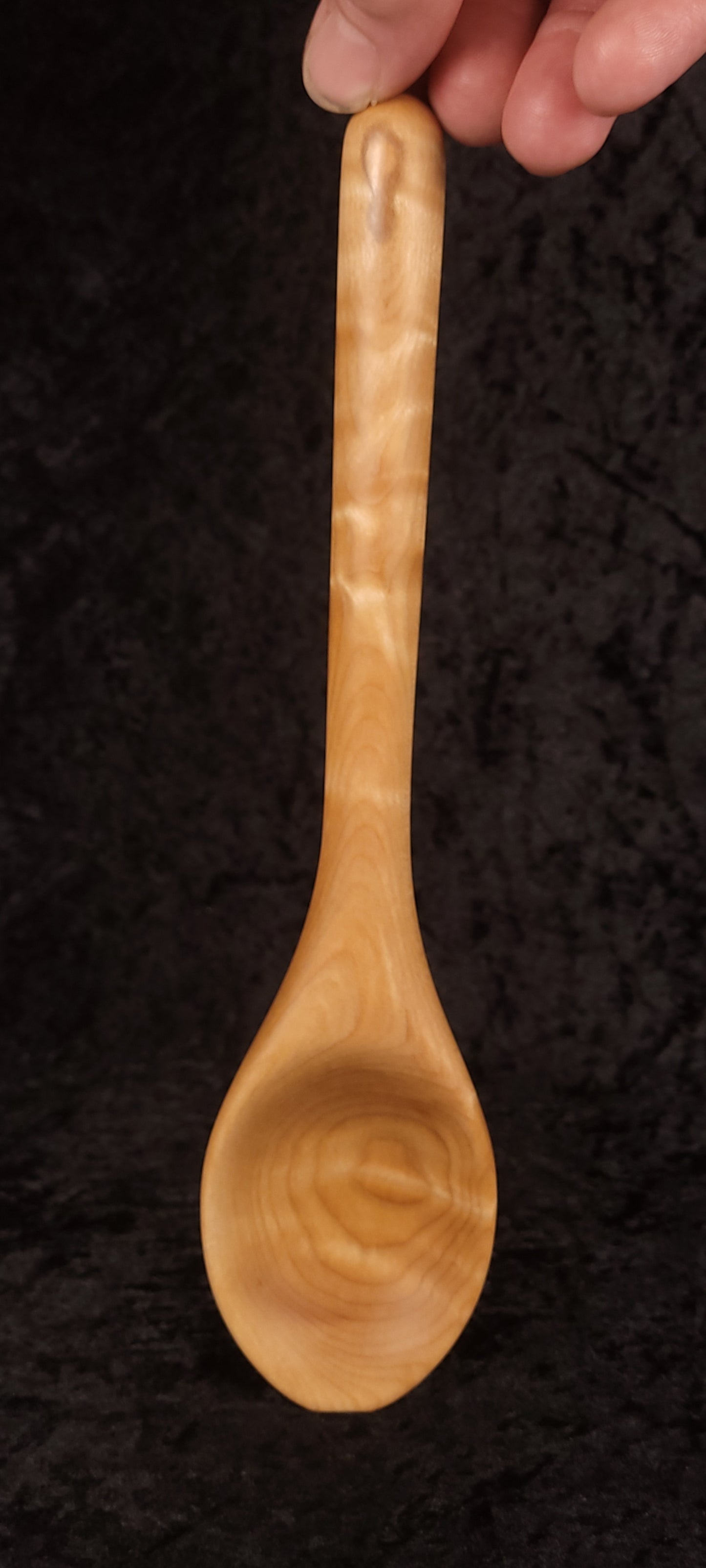 Curly maple spoon held up showing full length and figuring