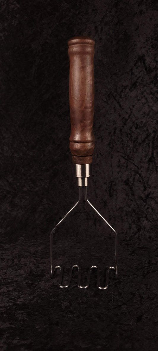 Handcrafted walnut potato masher resting on wood round, side view
