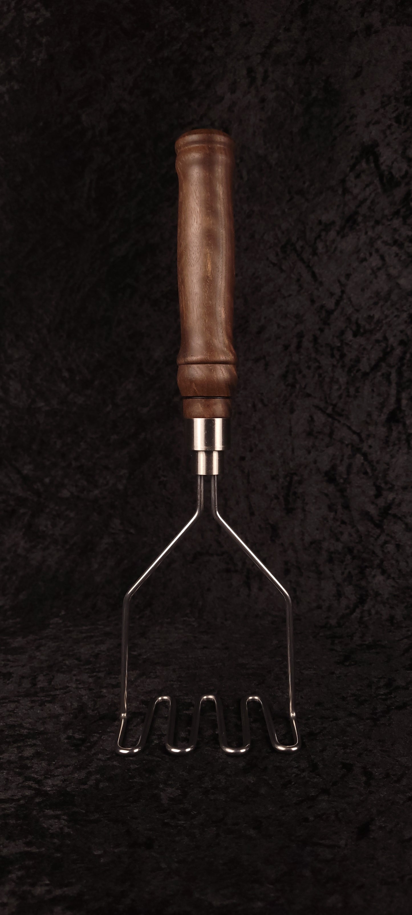 Walnut potato masher on wood round, alternate angle