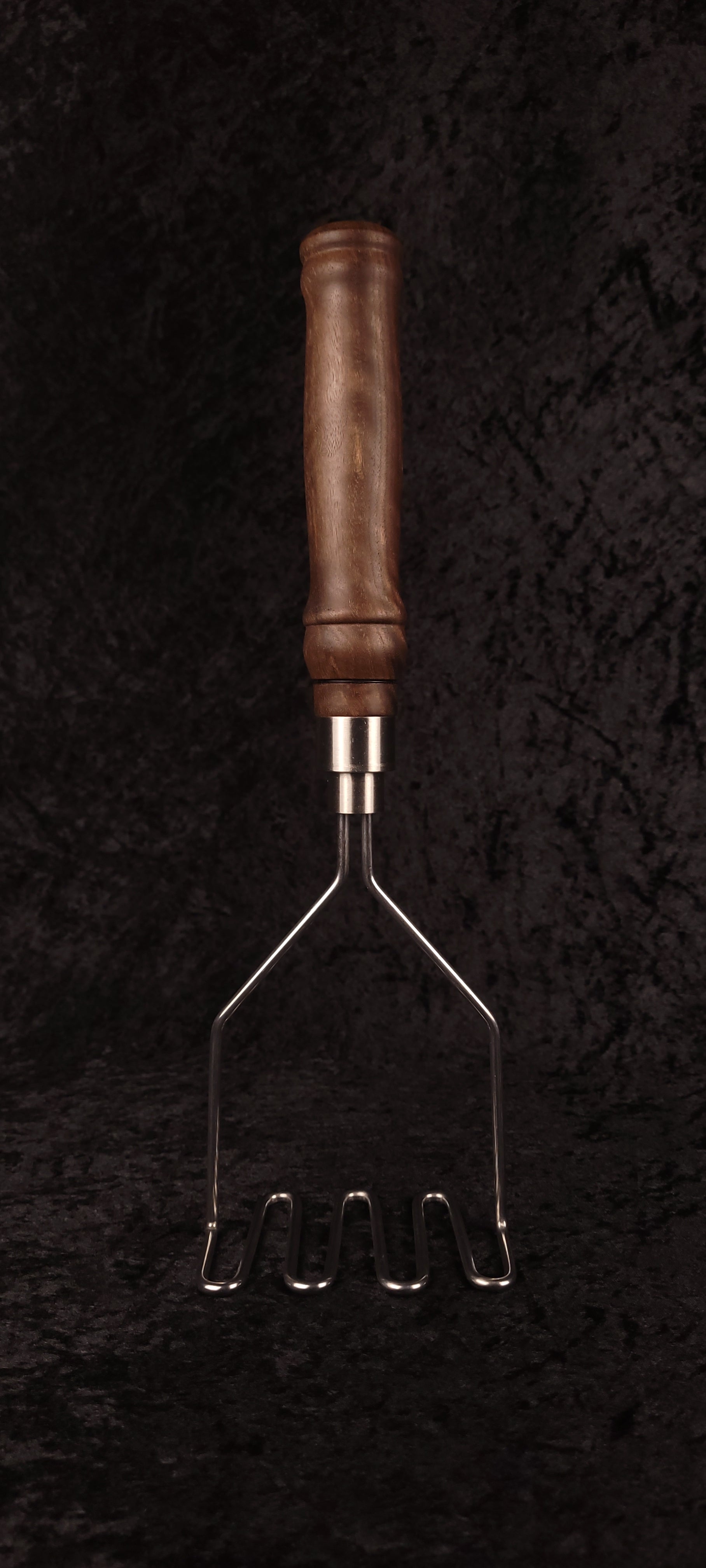 Walnut potato masher on wood round, alternate angle