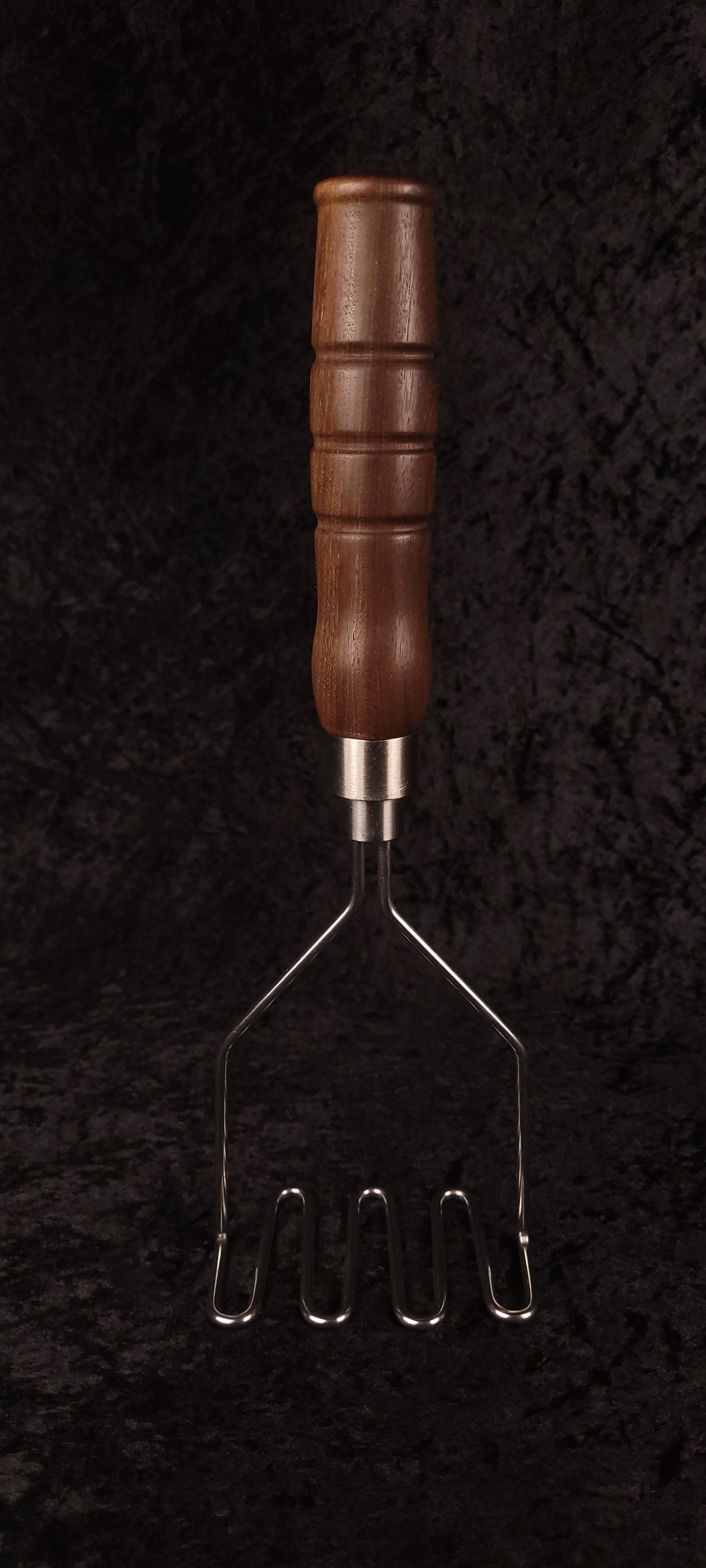 Walnut potato masher resting on wood round, side view