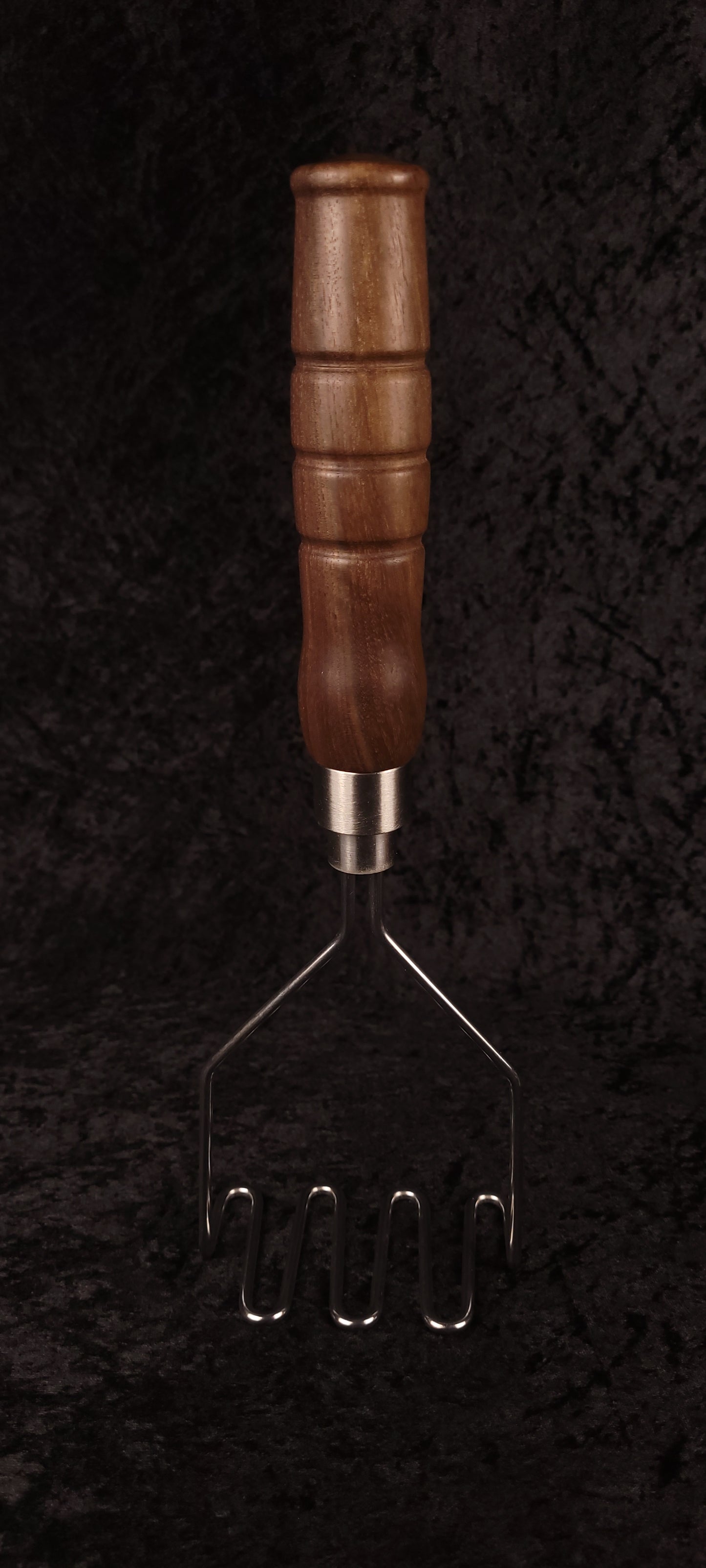 Walnut potato masher on wood round, alternate angle