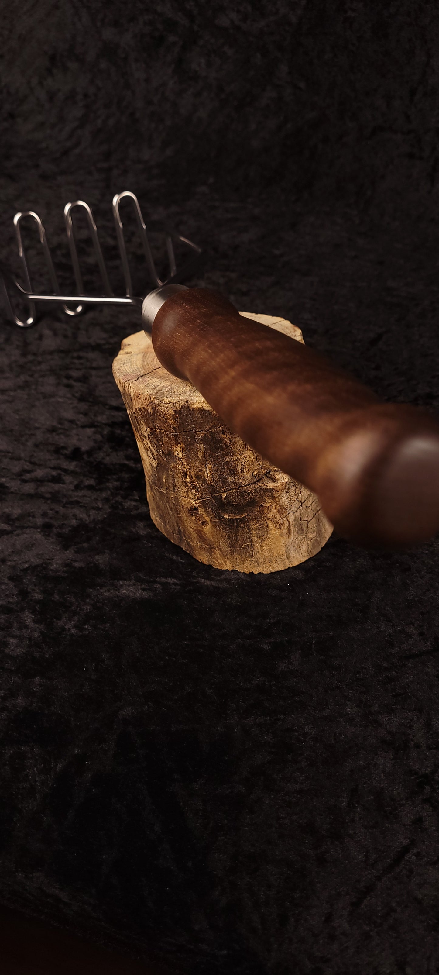 Handcrafted walnut potato masher resting on wood round, angled view showing wire head
