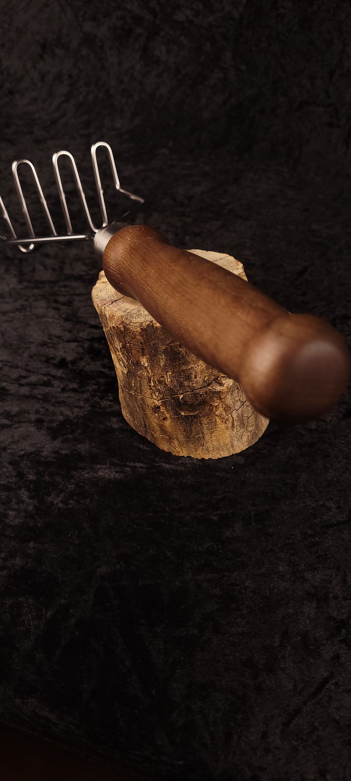 Walnut potato masher on wood round, alternate angle